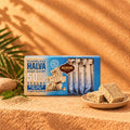 Halva ohne Zuckerzusatz: Geschenkpackung mit Riegeln, davor Halva-Stücke auf einem Holzteller