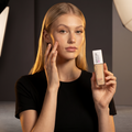 Model trägt Maybelline Superstay 24H Foundation auf die Wange auf und hält die Foundation-Flasche in der Hand