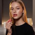 Maybelline Superstay Vinyl Ink Flüssiger Lippenstift, Model mit glänzend korallrosa Lippen im Studiolicht