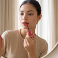 Model vor einem Spiegel beim Auftragen des Maybelline Superstay Vinyl Ink Lippenstifts in Pink